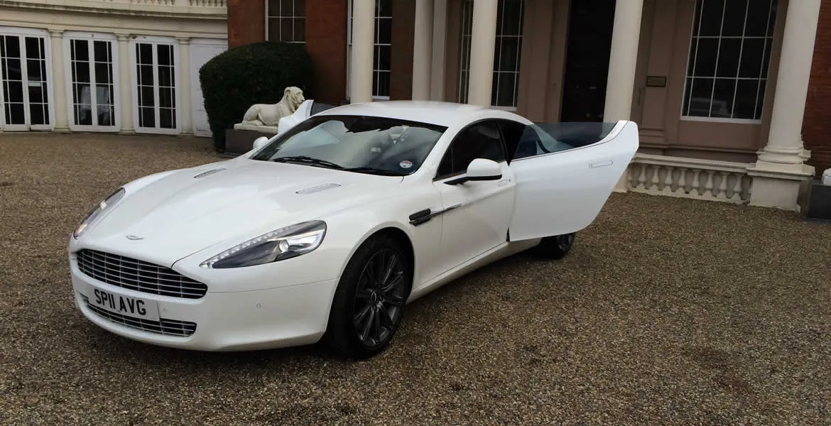 White Modern Aston Martin Rapide with 4-door in front of wedding venue with the doors open