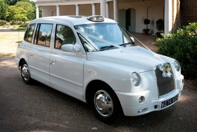 Modern White Taxi Cab dressed with white ribbons and bows on front grill waiting in front of wedding venue.