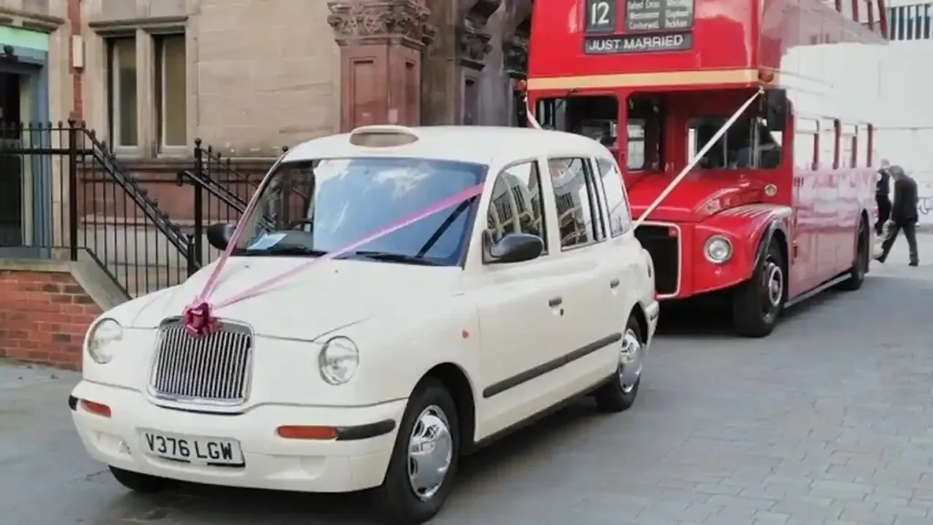 Modern White Taxi Cab decorated with Dark Pink Ribbons followed by a Double Decker Red Routemaster Bus in front of wedding venue
