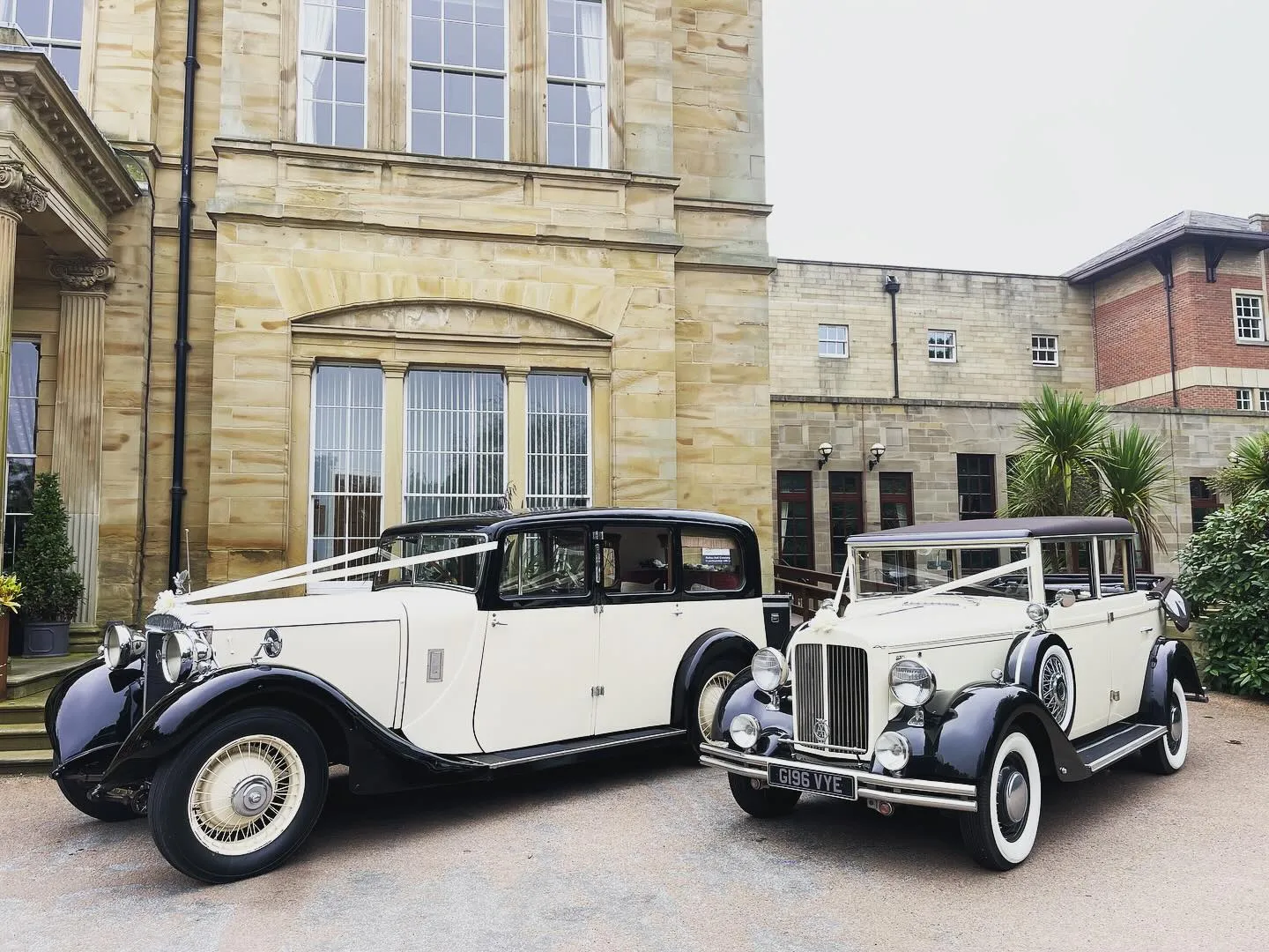 Two Large Traditional Old Limousine Wedding Cars dressed with Wedding Ribbons in front of wedding venue