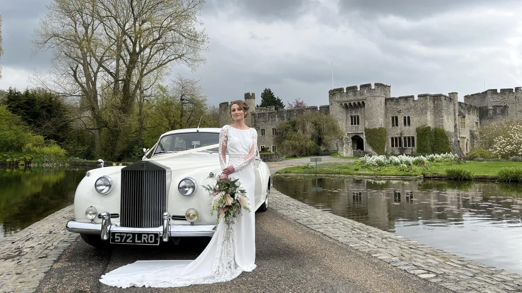 White Classic Rolls-Royce Silver Cloud in front of Wedding Castle with Bride holding flowers in her white dress
