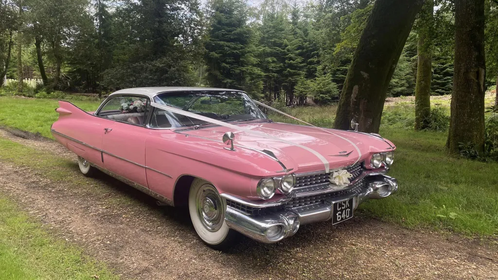 Classic Pink Cadillac with white ribbons accross the bonnet and large White wall tires