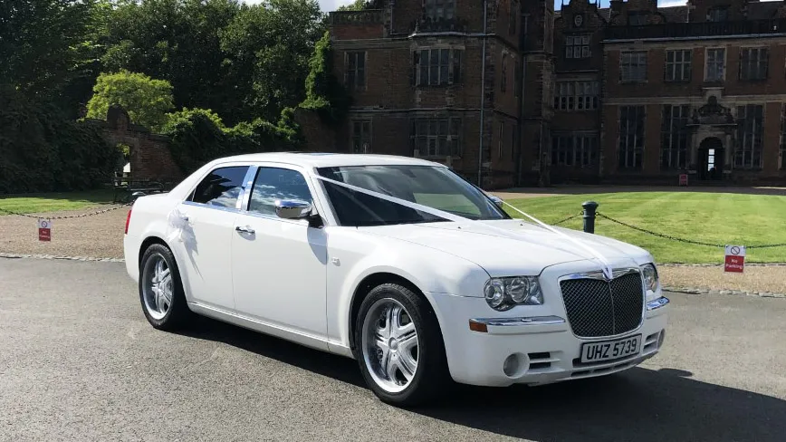 Side view of a White Modern American Chrysler 300c Saloon in front of wedding venue