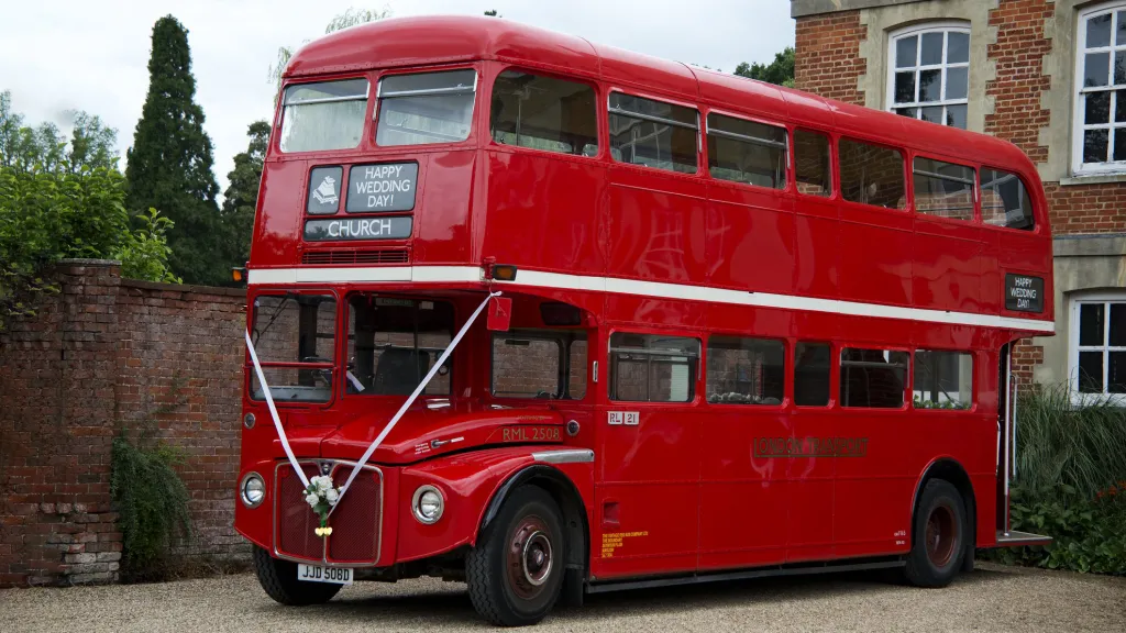Vintage Double Decker London Routemaster Bus decorated with white ribbons accross the front waiting outside wedding venue