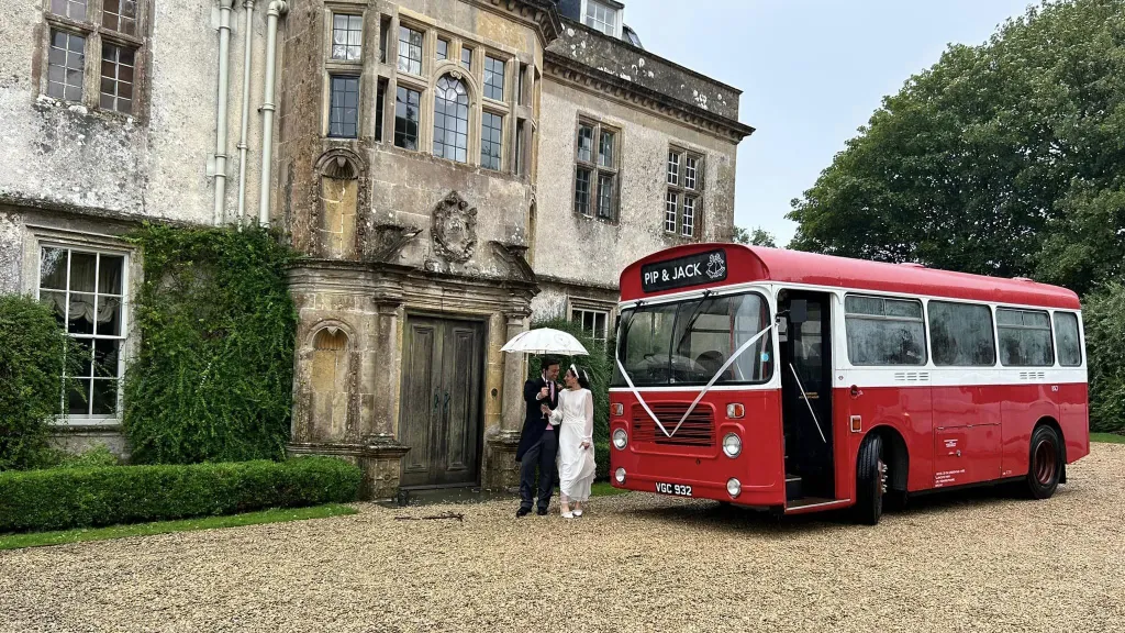 Classic Single Decker Wedding Bus in front of weddng venue with Bride and Groom in front of the bus holding a white umbrella