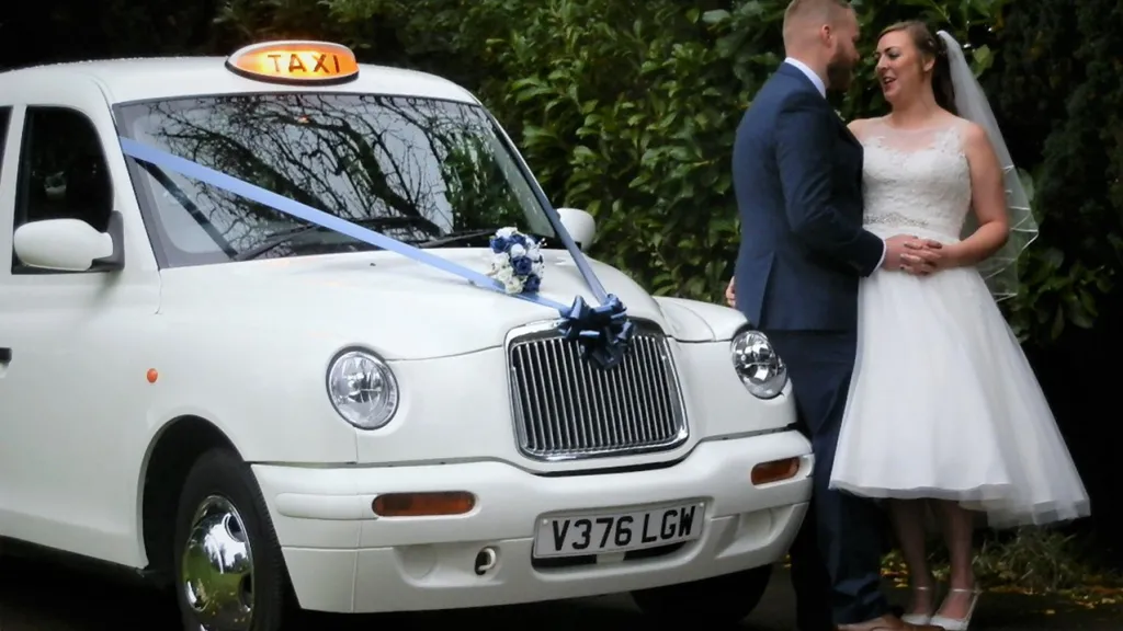 Bride and Groom standing by a white Taxi cab decorated with purple ribbon