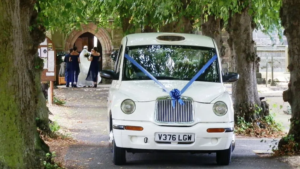 White Modern Taxi Cab entering wedding venue with lilac blue ribbons and bow on front grill