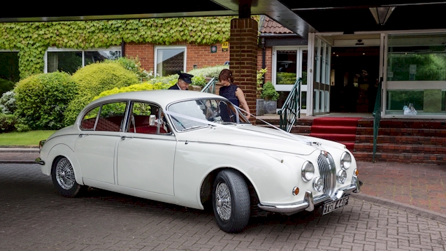 Classic Ivory Mk2 with wedding ribbons waiting outside the venue with a fully uniformed chauffeur.