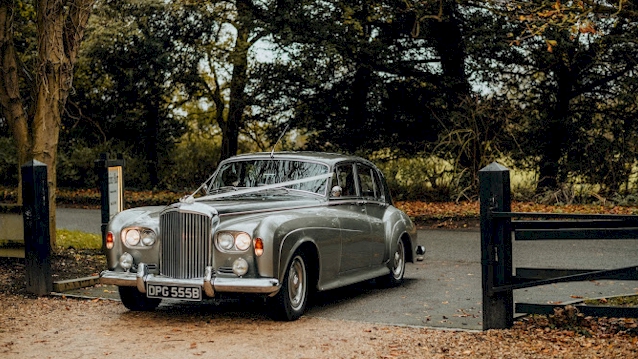 Classic Bentley S3 with twin headlights on entering a wedding venue and dressed with white ribbons