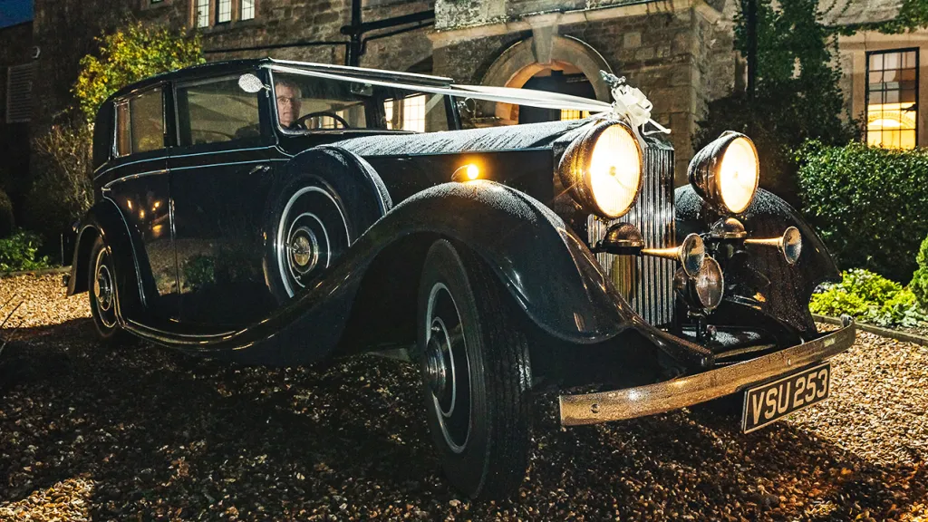 Vintage Rolls-Royce Sedanca with Wedding Ribbons at dusk with lights on in front of Pear Tree wedding venue in Purton