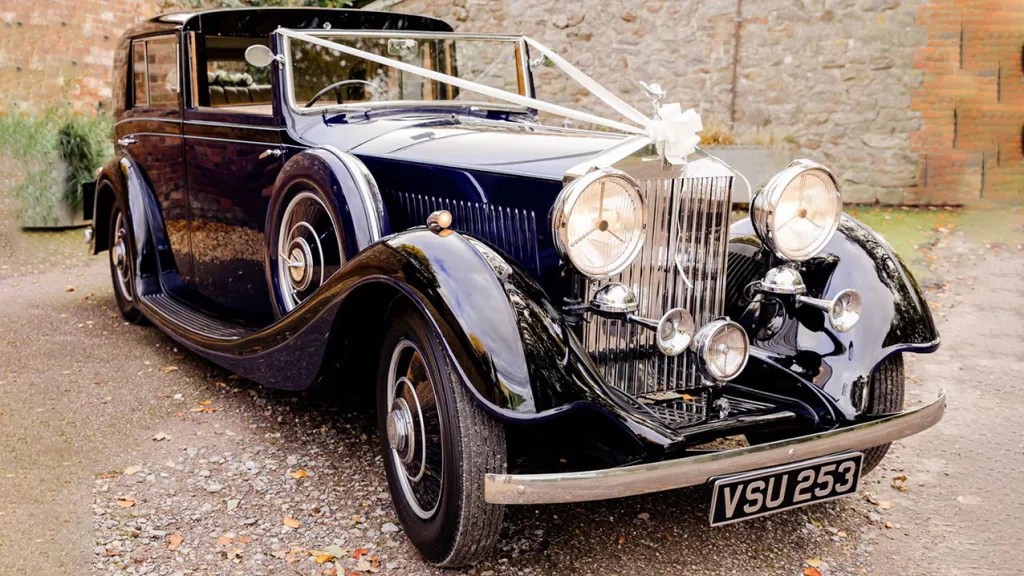 Front view of Blue Rolls-Royce showing the Large Chrime Grill, Traditional White ribbons accross the bonnet and White Bow on top of the front grill