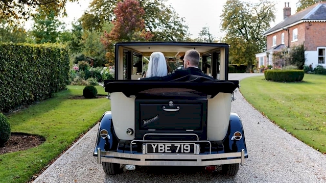 Rear view of vintage imprial car with roof down entering a wedding venue with bride and her father inside the vehicle