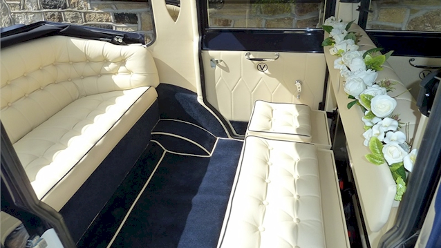 Rear inside seating area of imperial car showing both seats facing each others. Blue carpet and cream leather seats