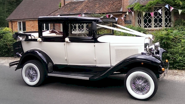 Right view of Black and White vintage Badsworth with roof down, white wall tires, and ivory ribbons accross the front of the vehicle