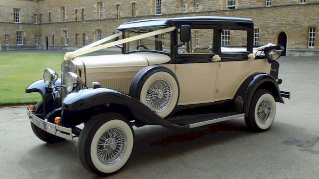 Front Left view of a Vintage Badworth wedding car with roof down decorated with white ribbons in front of a wedding venue