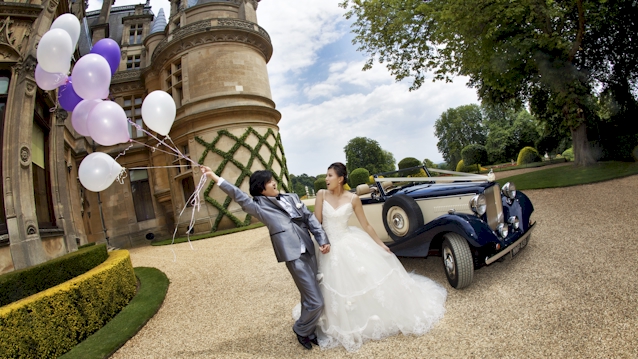 Bride and Groom standing in front of a vintage car for their wedding photos. Bride is wearing a large wedding dress