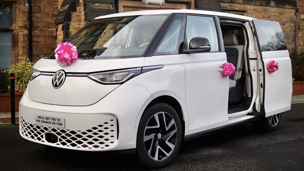 White Electric VW ID Buzz  with side rear door open and large Pink bows on the front of the car and door handles