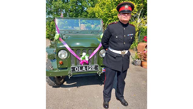 Chauffeur wearing a periood uniform in front of Classic Army Austin Champ Jeep decorated qwith Pink Ribbons