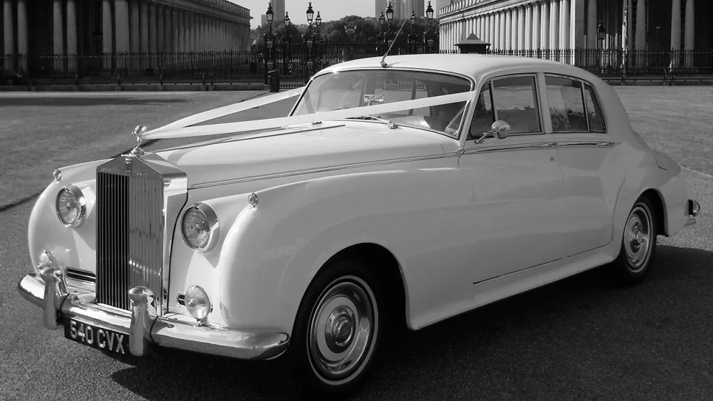 Black & White photo of a White Rolls-Royce Silver Cloud dressed with traditional wedding ribbons