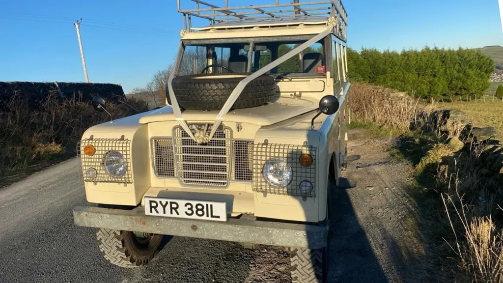 Front view of cream classic landrover showing the spare wheel mounted on the bonnet