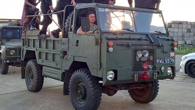 Side view of Khaki Green Classic Military Land Rover with chauffeur driving and passengers in rear