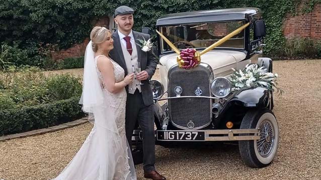Bride and Groom standing in front of a Bramwith on the day of their wedding. Car is decorated with Gold Ribbons and Red Bow
