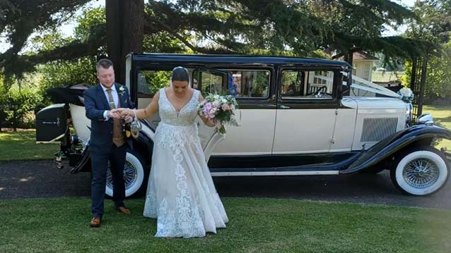Groom helping the Bride out of a Vintage Rolls-Royce while she is holding a White Wedding Flowers