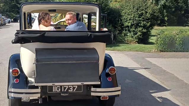 Rear view of Convertible Bramwith with Roof down and Bride and Groom seating in the rear seating looking back. Black picnic trunk fitted at the back of the vehicle