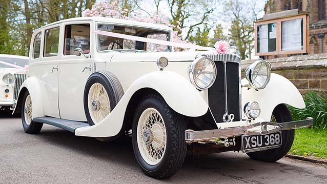 Side view of White Vintage Car in street waiting for Bride and decorated with ribbons