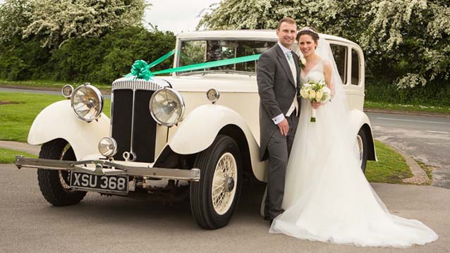 Bride and Groom standing in front of a Vintage Daimler decorated with turquoise blue ribbons and bows