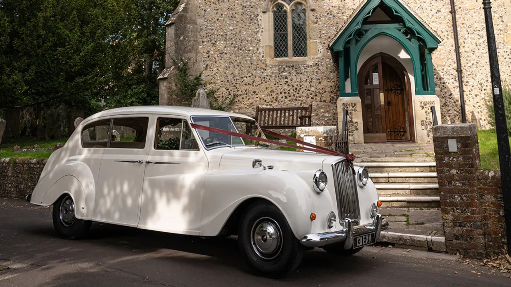 Right sde view of Classic wedding car decorated with burgundy wedding ribbon in front of church