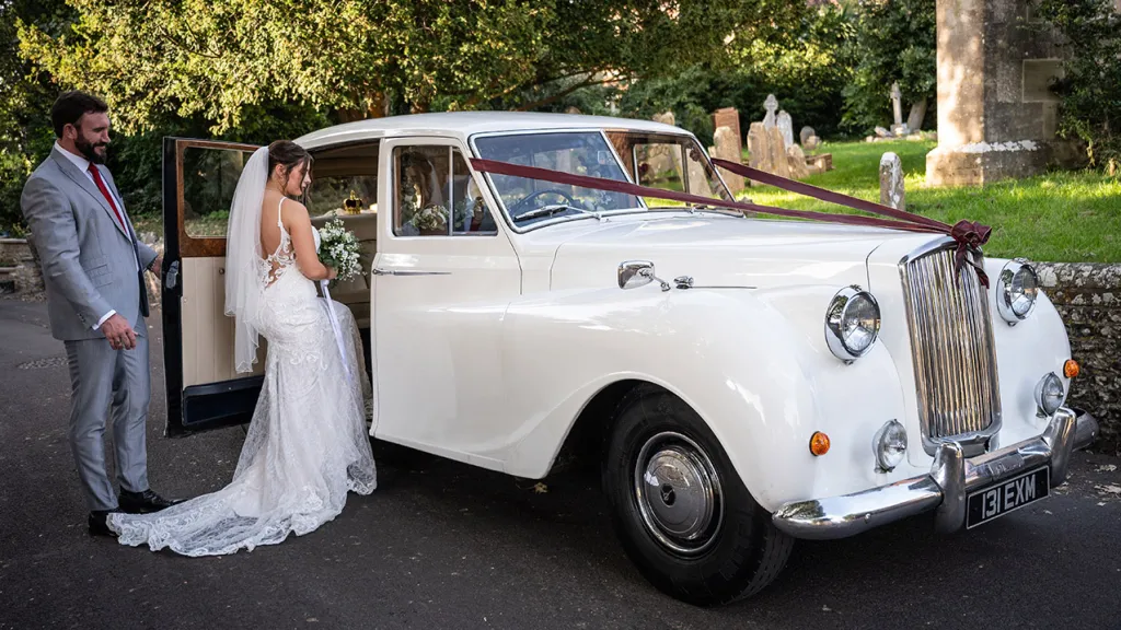 Bride entering classic Austin car while Groom holds the door open.