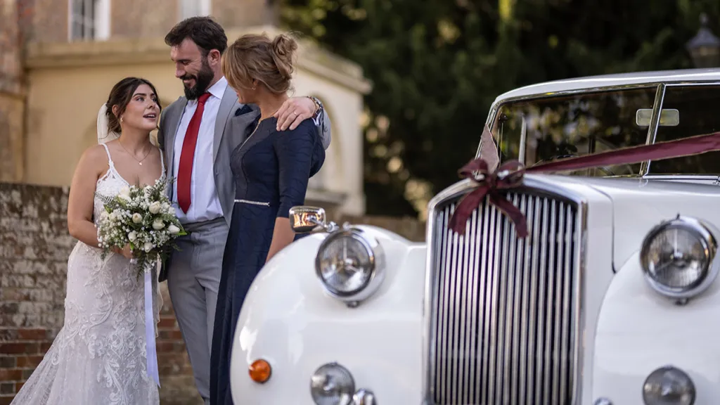 Happy Wed couple standing by the classic Austin car hired on their wedding day