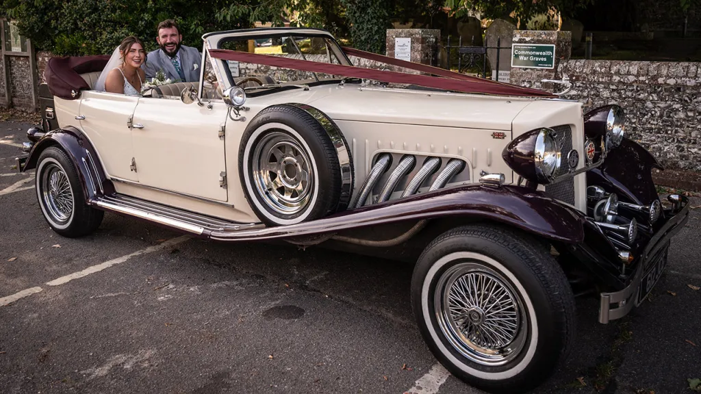 Bride and Groom seating in rear of a vintage wedding car with roof down