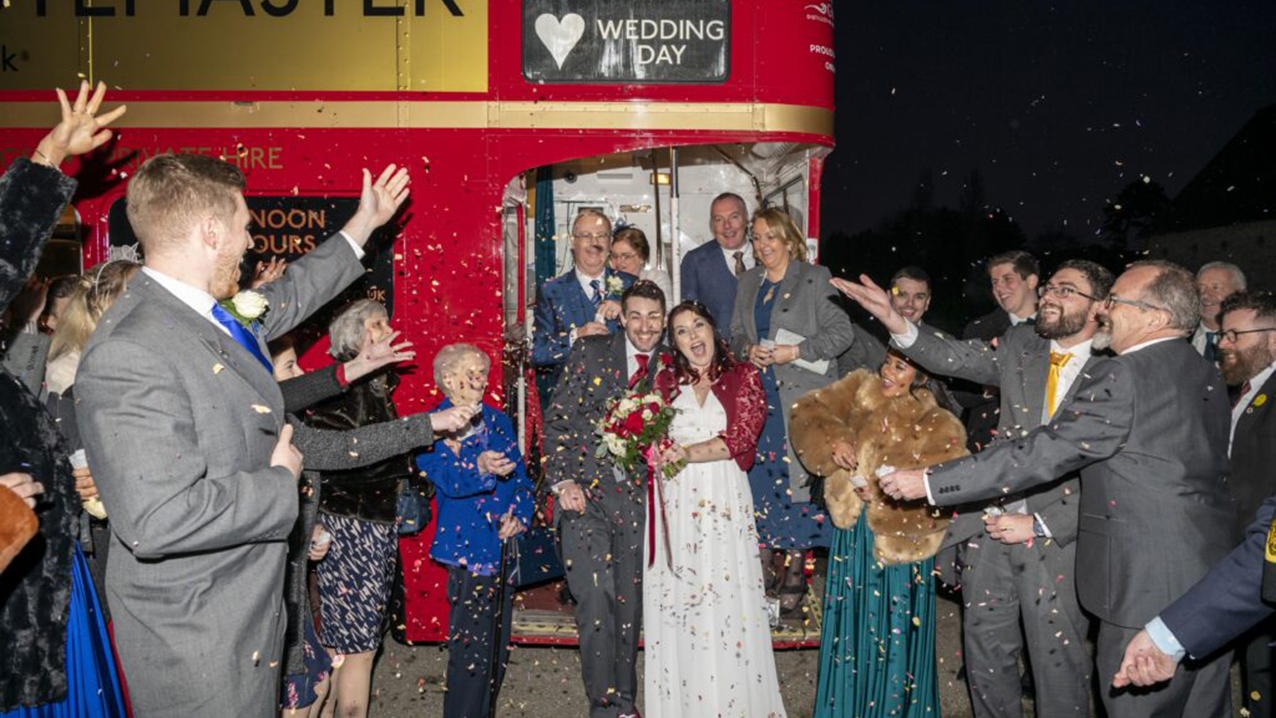 Wedding Party throwing confettis at Bride and Groom coming out of the Red Routemaster bus
