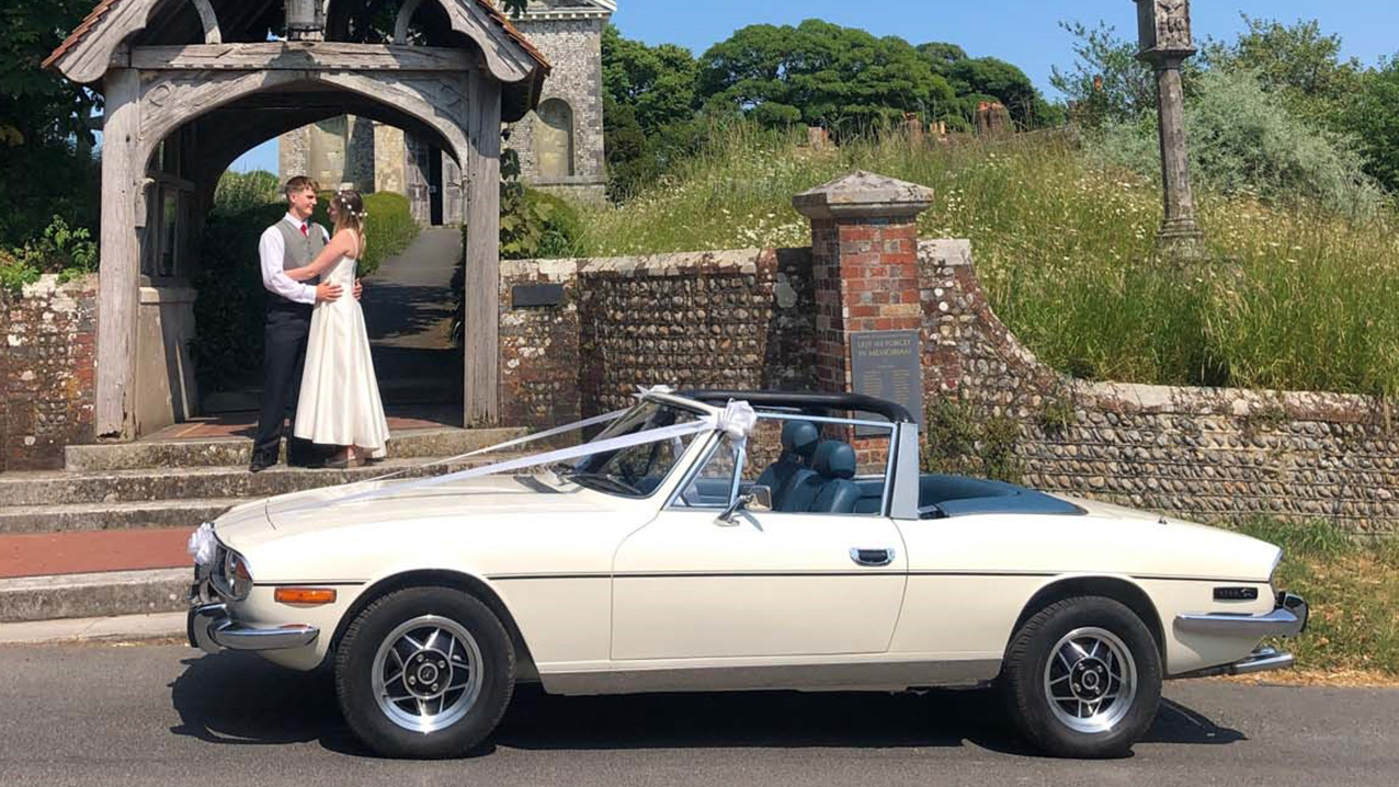 left view of Classic Triumph dressed with wedding ribbons in front of a church with Bride and Groom in the background
