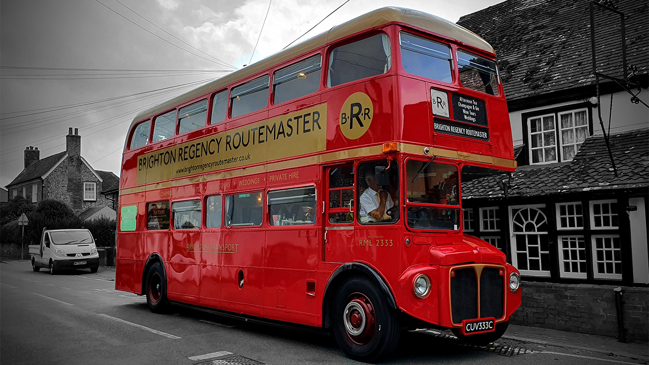 Side view of Red Routemaster bus in Red with in a Black & White Background showing old Cottage house