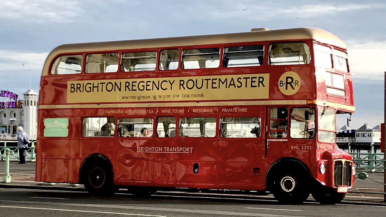 Red Routemaster bus on Brighton Sea Front showing a busy pier in the Background