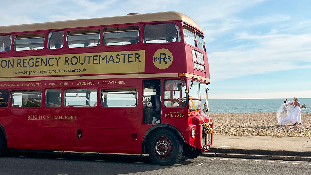 Red Bus on Sea Front with two brides walking on the sandy beack in the background
