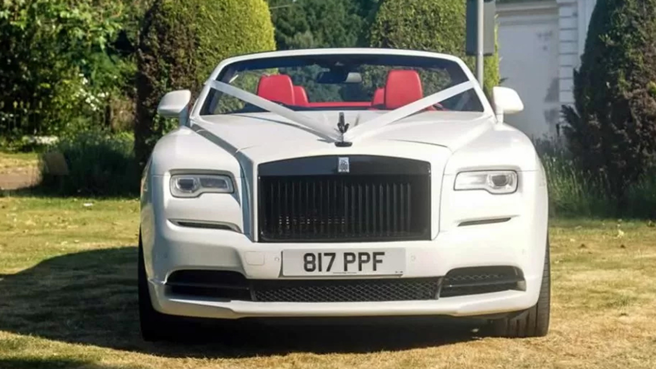 Front view of White Modern Rolls-Royce Dawn with White ribbon accross its bonnet going over the spirit of ectasy