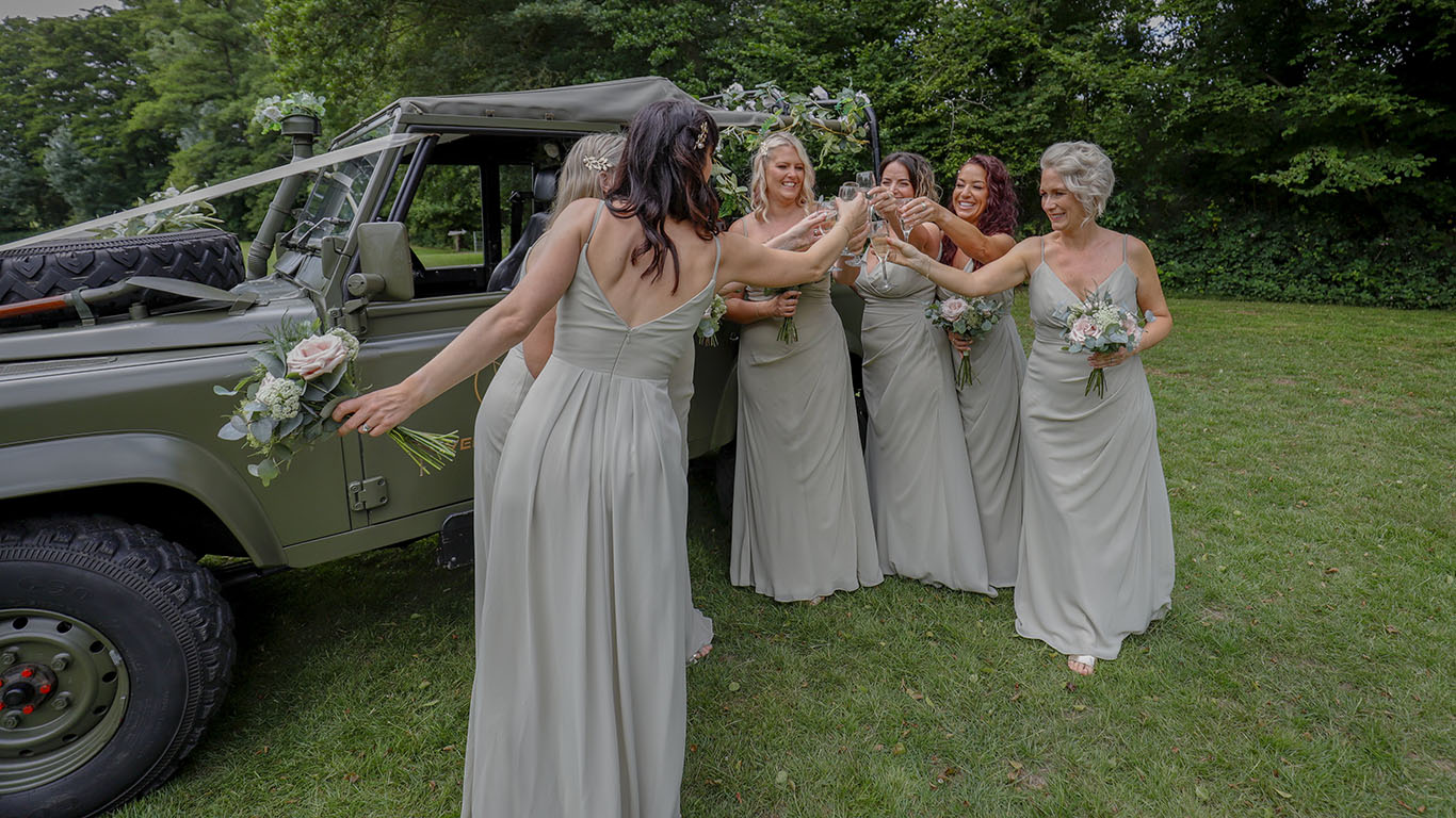 Bridesmaids wearing a pale green dressed cheering in Front of Landrover decorated with wedding ribbons