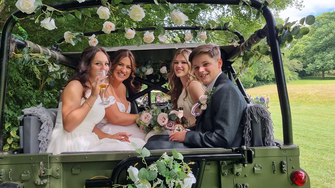 Bridesmaids and Page boy seating in the rear of the Landrover with Canvas roof open and decorated with White Wedding Flowers