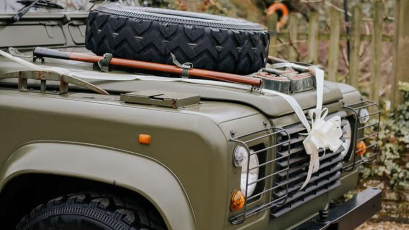 White Ribbon and bow on the front grill of the Khaki Green Military Landrover Vehicle. Spare wheel mounted on bonnet