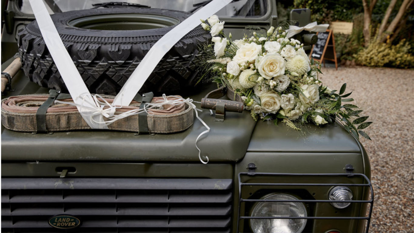 White Ribbon and wedding flower on the front grill of the Khaki Green Military Landrover Vehicle. Spare wheel mounted on bonnet