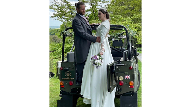 Bride and Groom holding each others standing up in the back of the Military Landrover with its canvas roof open