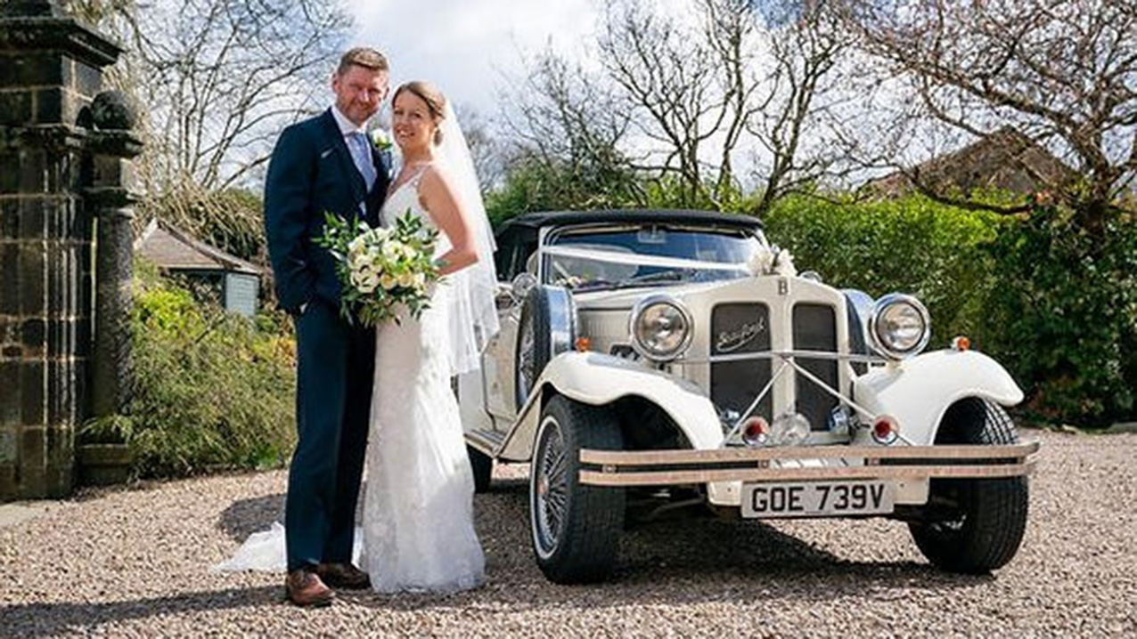 Bride and Groom standing ion front of the Beauford Wedding Car, posing for their photographer
