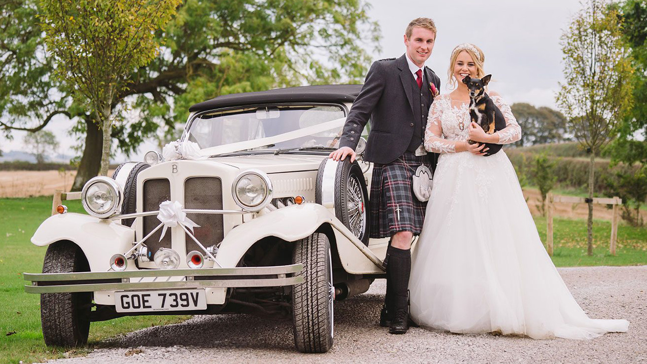 Beauford Convertible with Black roof and Ribbons with bride and groom standing by the vehicle