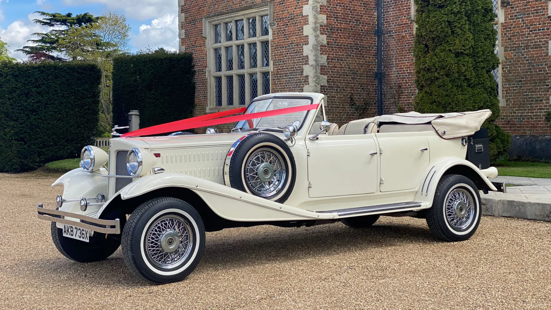Ivory Convertible Beauford in front of a wedding venue decorated with traditional "V-Shape" ribbons in Red accross its bonnet