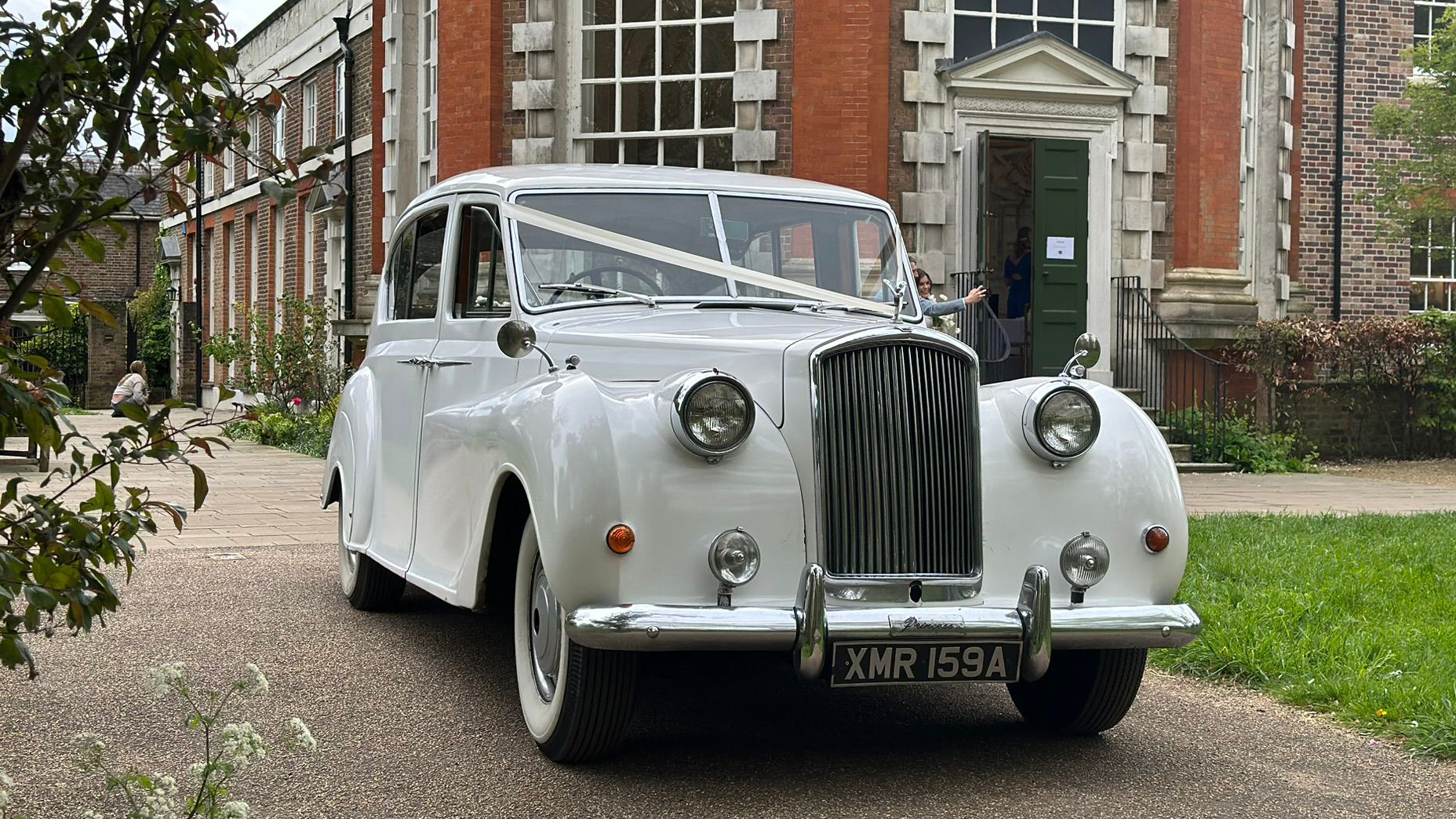 Front view of Classic Asution Princess decorated with white ribbons accross its bonnet leaving wedding venue in Essex