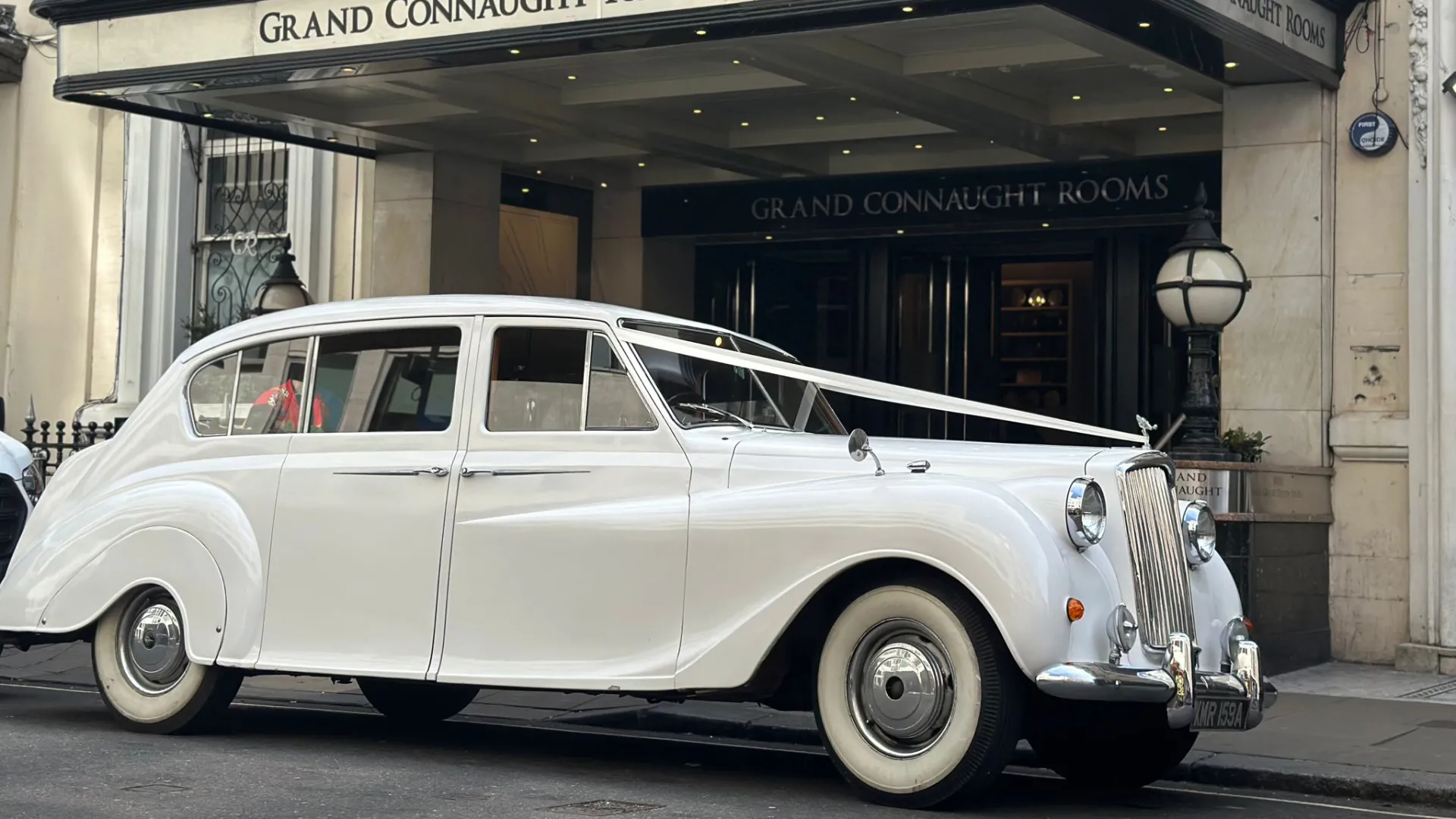 Side view of Classic Austin princess decorated with white wedding ribbons waiting outside Grand Connaught Hotel in London